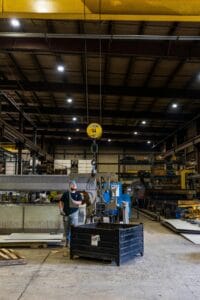 Butler Holding Company An industrial worker operates a crane in a spacious factory warehouse, surrounded by machinery.